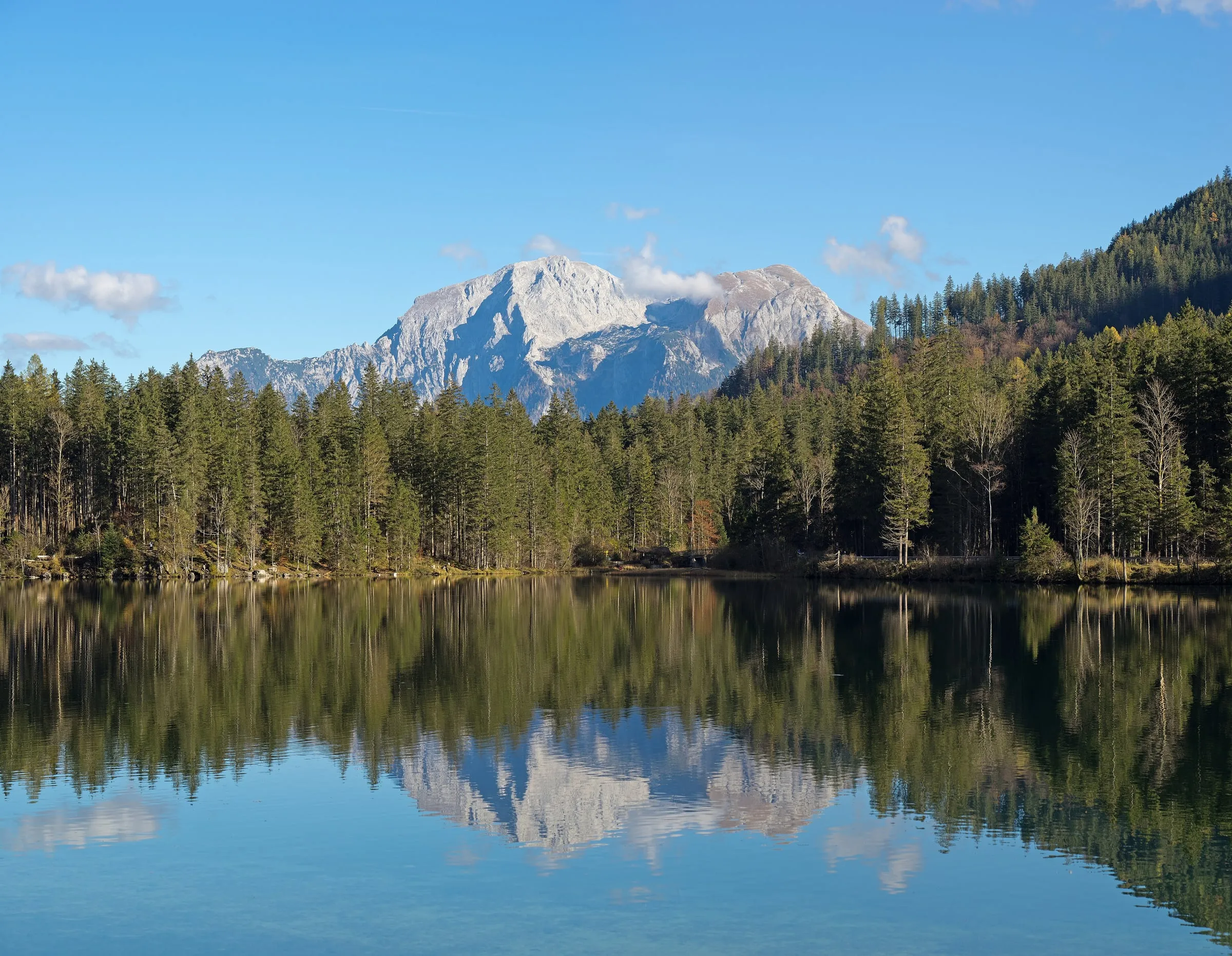 Ein Bergmassiv spiegelt sich in einem stillen Bergsee, umgeben von Nadelwald.